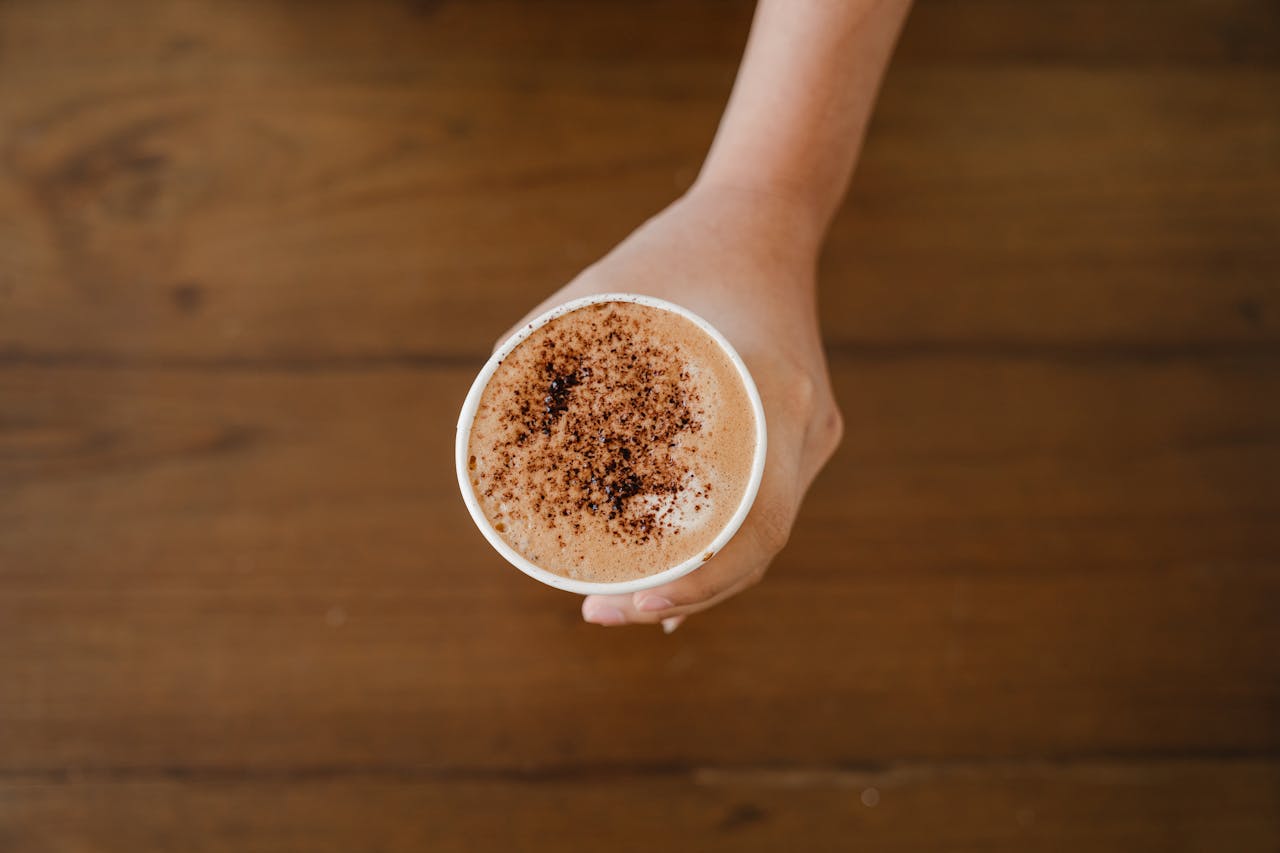 A hand holding a cappuccino cup topped with cocoa powder, captured from above.